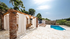 A covered outdoor area with a pool, brick pillars, and a stone wall.