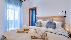 Ein ordentlich bezogenes Bett mit zwei aufgerollten Handtüchern, einem hölzernen Kopfteil und einer Nachttischlampe.