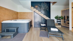 Ein modernes Badezimmer mit einer freistehenden Badewanne, einem schwarzen Loungesessel mit Handtuch und einer Treppe mit dekorativem Blattmuster.