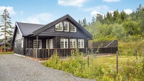 Une cabane en bois avec un toit à forte pente, de grandes fenêtres et une allée gravillonnée.