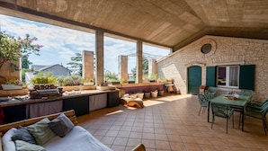 Eine geräumige Terrasse mit Steinmauer, Essbereich und einer Sitzecke mit Kissen und einer Couch.