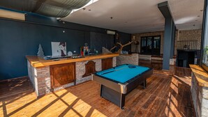 Ein Billardtisch in einem Raum mit Backsteinwand, Barbereich und einem großen Fenster.