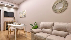 Un salon avec un canapé beige, une table à manger avec des chaises, un téléviseur fixé au mur et un miroir décoratif.