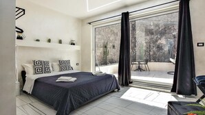 Une chambre moderne avec un grand lit, un balcon doté d’une table et de chaises, et une vue sur l’extérieur.