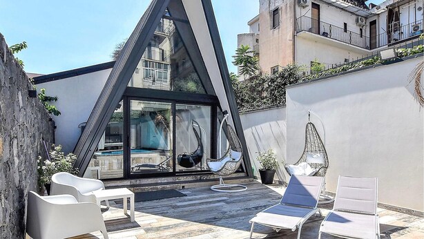 Une terrasse moderne sur le toit, dotée d’une structure vitrée, de chaises longues blanches et d’un fauteuil suspendu.