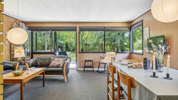 A modern interior with a dining area, a sofa, and a view of greenery through large windows. - 3 bedroom stunning home in Hasle (Hasle)