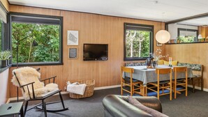 A modern room with wooden panel walls, a dining area with a table and chairs, a sofa, a rocking chair, and a television mounted on the wall. - 3 bedroom stunning home in Hasle (Hasle)
