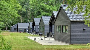Een rij vakantiehuisjes met puntige daken, buiten zitplaatsen en een barbecue op het terras.