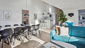 Een moderne woonkamer met een blauwe bank, een eethoek met stoelen en een keuken met witte kasten.