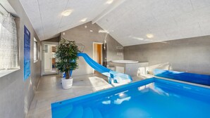 Een binnenzwembad met een blauwe glijbaan, een potplant en een moderne badkamer.