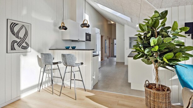 Een moderne keuken met witte kasten, een eethoek met twee grijze stoelen en een grote potplant.