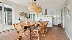 A spacious dining area with a large wooden table and wicker chairs, a modern kitchen in the background, and a brick floor. - Nice home in Fjerritslev with WiFi (Fjerritslev)