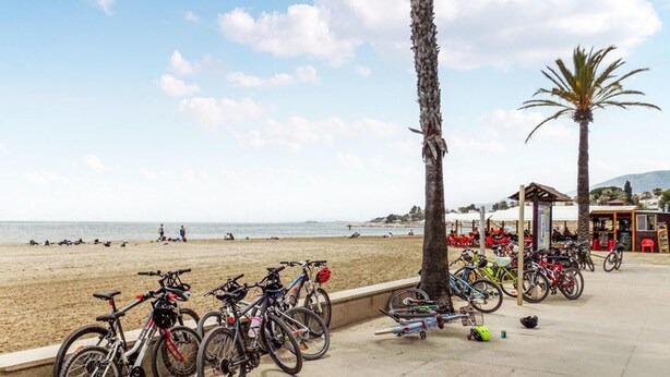 Ein Strand mit Fahrrädern am Ufer, einer Kiosk und Palmen.