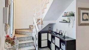 Eine Treppe mit weißen Geländern, ein schwarzer Konsolentisch mit Schubladen sowie ein an der Wand befestigtes Regal mit Pflanzen und Bildern.