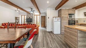 Una cocina moderna con vigas de madera, un comedor con mesa y sillas, y una pared de piedra.