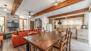 Amplia sala de estar con una mesa de comedor de madera, asientos tapizados en rojo, un muro de piedra y una cocina con electrodomésticos modernos.