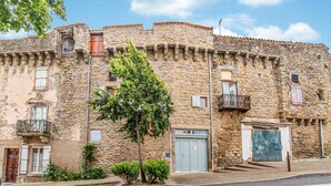 Un edificio de piedra con varias ventanas y puertas, un árbol en primer plano y un cielo despejado.