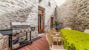 Un espacio al aire libre con paredes de piedra, una parrilla, sillas y una mesa con mantel verde.
