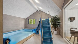 An indoor swimming pool with a blue slide and stairs, a potted plant, and a glass door leading to a dining area. - Cozy home in Krakow am See with sauna (Krakow am See)