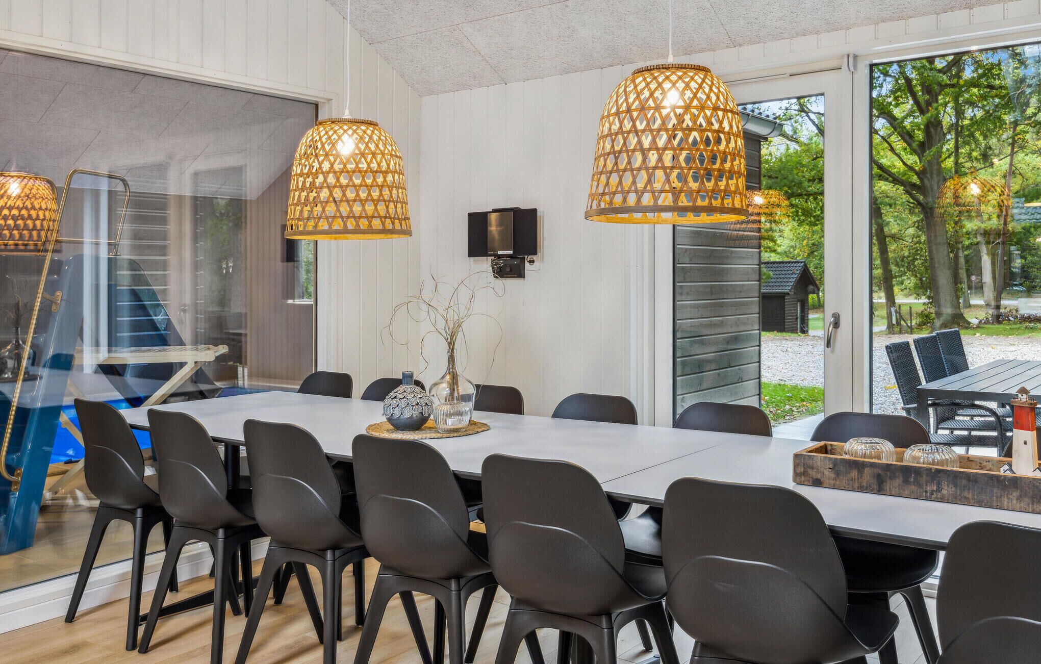 Un comedor moderno con una mesa grande, sillas negras y lámparas colgantes de mimbre.