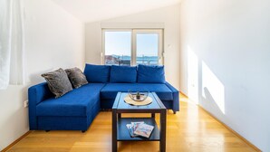 Una sala de estar moderna con un sofá seccional azul, una mesita con revistas y vistas a la ciudad a través de amplios ventanales.