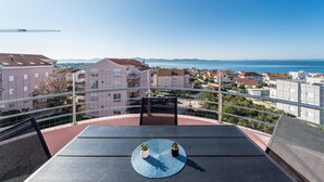 Un balcón con mesa y sillas, con vistas a un pueblo costero con edificios y el mar.