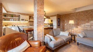 A modern living room with leather sofas, a dining area, and a kitchen with brick walls. - Lovely home in Castiglione Del Lago (Castiglione Del Lago)