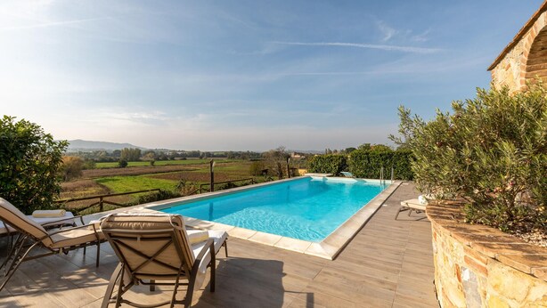 A swimming pool with lounge chairs, a stone wall, and a view of the countryside. - Lovely home in Castiglione Del Lago (Castiglione Del Lago)