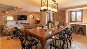 A spacious living room with a wooden dining table, multiple chairs, a sofa, and a television mounted on the wall. - Lovely home in Castiglione Del Lago (Castiglione Del Lago)