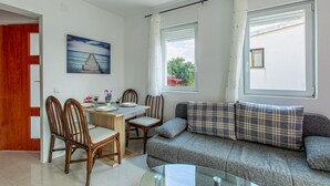 Un comedor con una mesa dispuesta para dos personas, dos sillas de madera, un sofá gris con cojines de cuadros y un cuadro de un muelle en la pared.