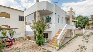 Un edificio de dos pisos con fachada de piedra, una escalera y un pequeño espacio al aire libre con una mesa y sillas.