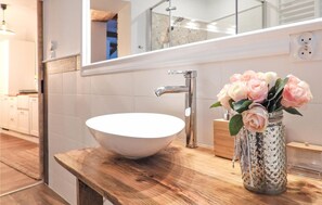 Een badkamer met een witte wastafel, een moderne kraan en een decoratieve vaas met bloemen.