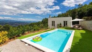 Ein modernes Haus mit Swimmingpool, umgeben von üppiger Vegetation und einem malerischen Blick auf ferne Berge.