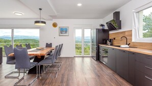 Eine moderne Küche mit einem Holzespeisetisch, grauen Stühlen und Blick auf die Berge durch große Fenster.