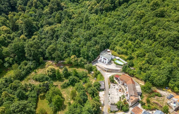 Une vue aérienne d’un complexe hôtelier isolé, avec un bâtiment central entouré d’une forêt dense, comprenant une piscine et plusieurs chambres pour les clients.