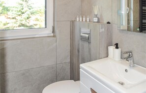 Een moderne badkamer met toilet, wastafel en douche. Toiletartikelen staan op een plank en boven de wastafel hangt een spiegel.