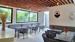 A modern dining area with wooden ceiling beams, large windows, and black wicker chairs. - BT Rooms Tulum (Tulum)