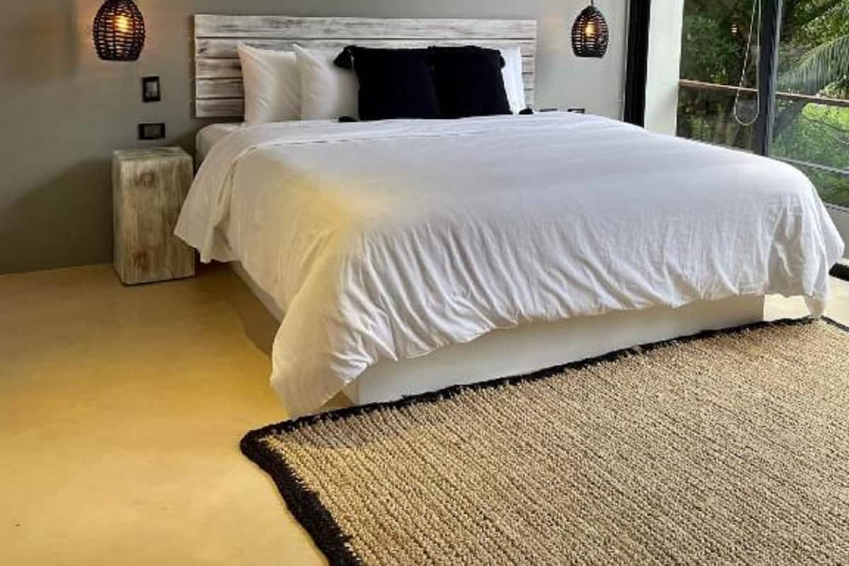 Ein modernes Schlafzimmer mit einem großen Bett, einem Holzkopfende und Blick auf Grün durch große Fenster.