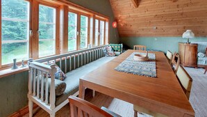 Una sala da pranzo in legno con un tavolo lungo, panche e vista sull'esterno attraverso ampie finestre.