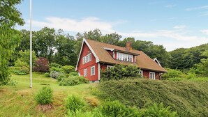 Una casa rossa con tetto spiovente, immersa nel verde e alberi.