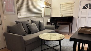Una sala de estar con un sofá gris, una mesa de centro redonda, un escritorio con una silla y una puerta blanca.