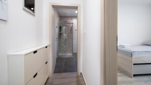 Een smalle gang die leidt naar een badkamer met een douche en een bed met een stippenbed overtrek.