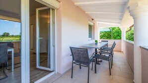 Een balkon met een eettafel en stoelen, een schuifpui en uitzicht op groen.