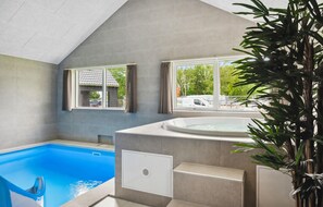 Ein moderner Innenpool mit Whirlpool, großen Fenstern und Blick ins Freie.