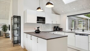 A modern kitchen with white cabinetry, a central island, black pendant lights, and a view of the outdoors through a window. - Beach front home in Krakow am See (Krakow am See)