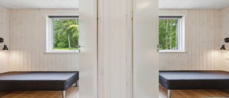 Une pièce aux murs recouverts de miroirs, avec un banc, deux fenêtres et un plancher en bois.