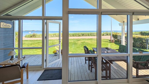 A room with large windows offering a view of a grassy area and the sea. - 2 bedroom beach front home in Sjølund (Sjølund)