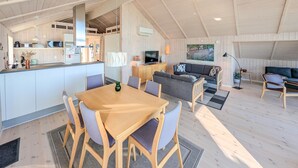 A spacious living area with a dining table, sofa, and kitchen in the background. - 2 bedroom beach front home in Sjølund (Sjølund)