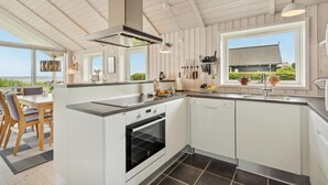 A modern kitchen with white cabinets, a built-in oven, and a large window offering a view of the outdoors. - 2 bedroom beach front home in Sjølund (Sjølund)