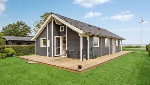 A single-story house with a grey exterior, a wooden deck, and a small patio area. - 2 bedroom beach front home in Sjølund (Sjølund)